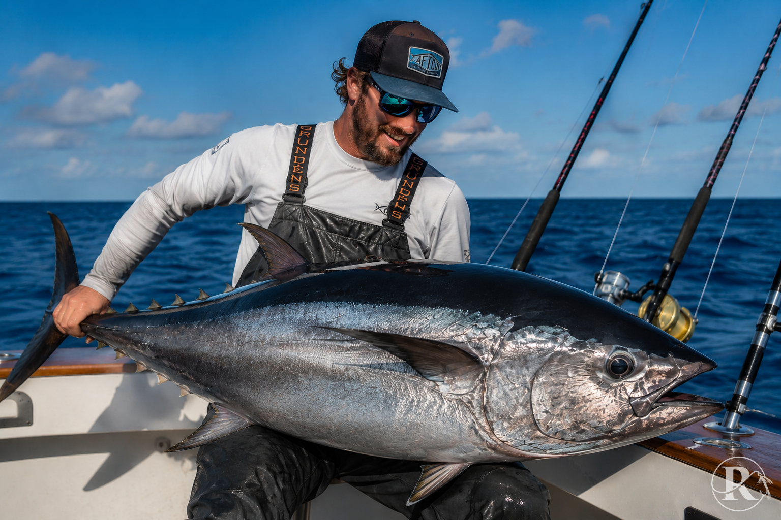 An angler holding a large bluefin tuna on the deck of an offshore fishing charter boat under a clear blue sky.