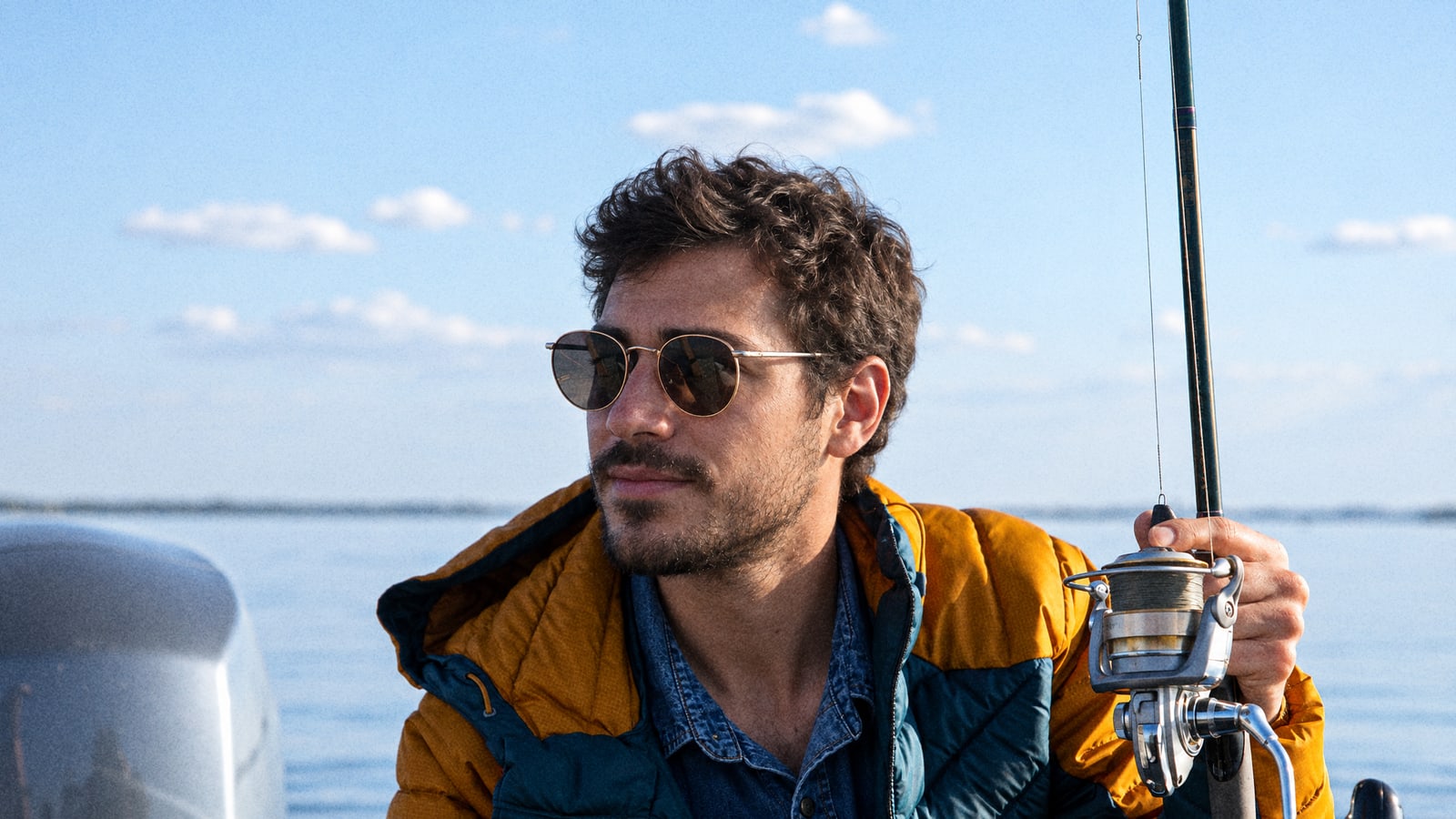 An angler in a warm jacket holding a rod on a small boat at sea