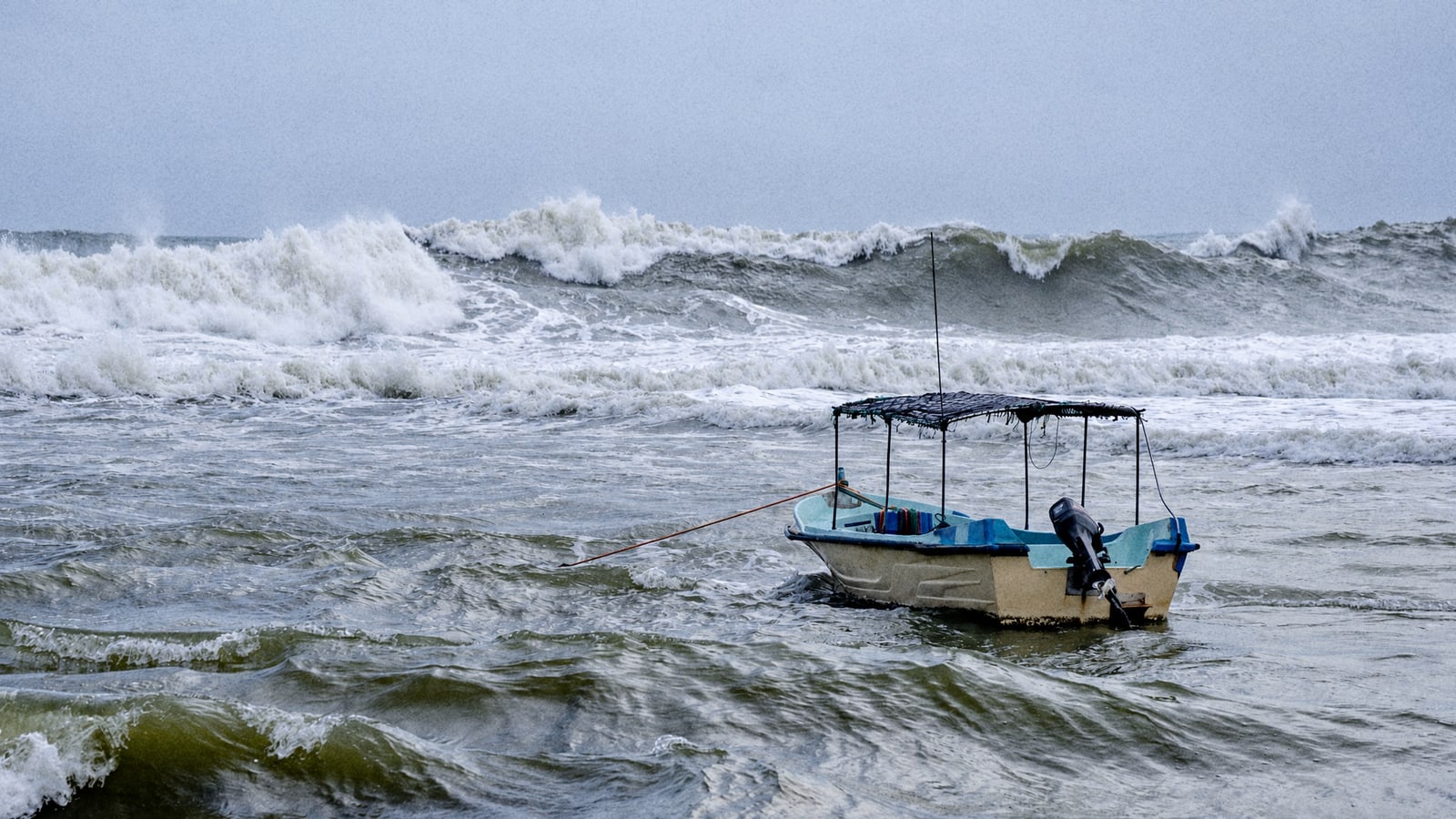 A small canopy fishing boat moored in rough surf on a grey windy day, the kind of morning a captain calls the trip off