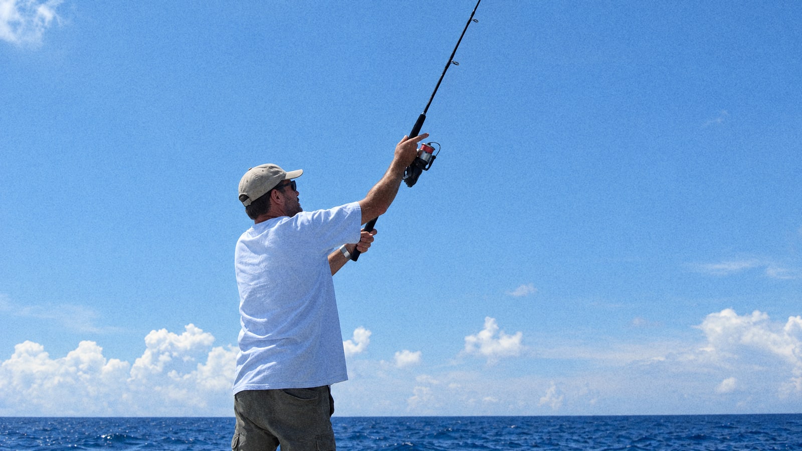 Angler casting from the deck of a fishing boat under a clear blue sky