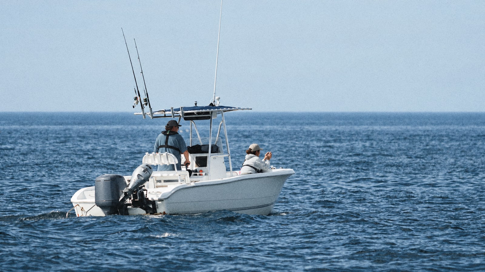 Two anglers on a small centre console fishing boat out on a lightly rippled blue sea