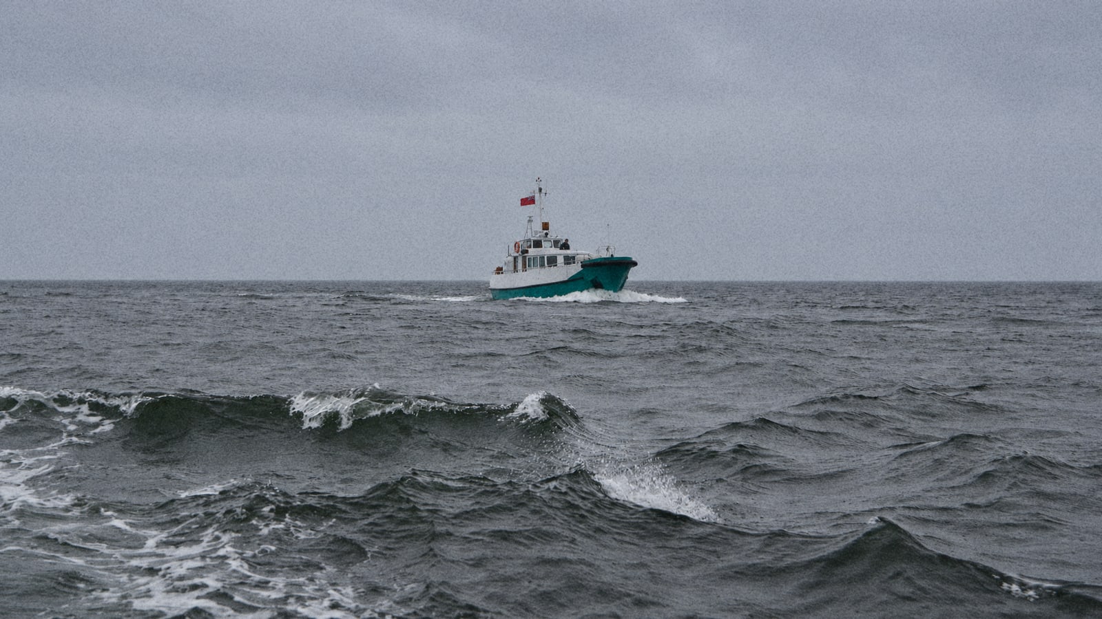 A small fishing boat heads out through grey, choppy sea under an overcast sky